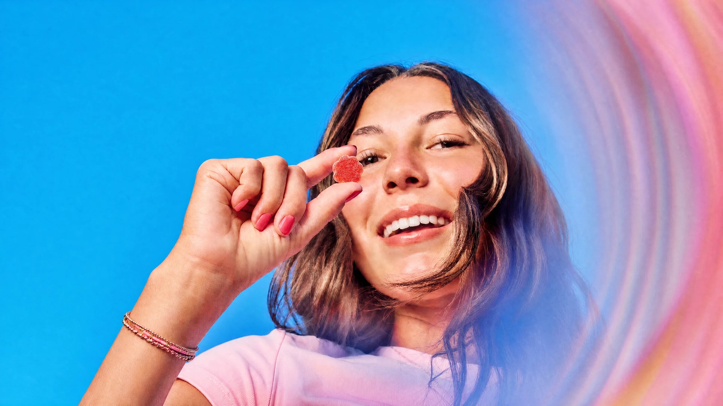 Woman holding a single red gummy against a bright blue sky
